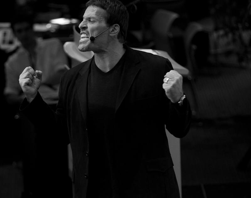 Tony Robbins no palco, punhos cerrados, falando para a plateia
